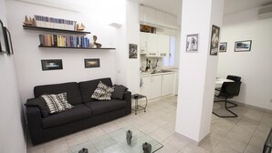 A modern living room with a black sofa, a glass coffee table, and a kitchen in the background. - Appartamento Bilo Amore (Portoferraio)