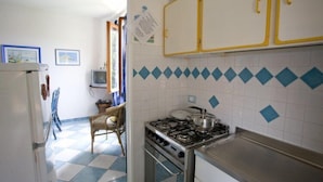 A kitchen with a gas stove, white cabinets with yellow handles, a checkered floor, and a television in the background. - Appartamento Casa Paoletta (Rio)