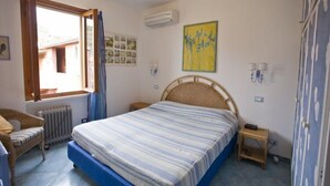 A bedroom with a bed, a chair, a small table, an air conditioner, and a window with curtains. - Appartamento Casa Paoletta (Rio)