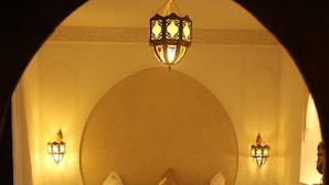 Un dormitorio con una cama grande, dos lámparas de noche, una mesita de noche, un cofre decorativo y un arco de entrada.
