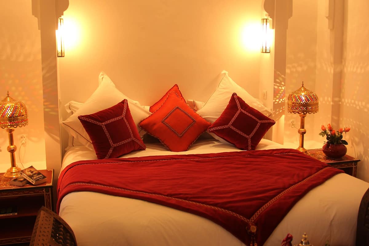 A bed with a red blanket, pillows, and a tray with snacks.