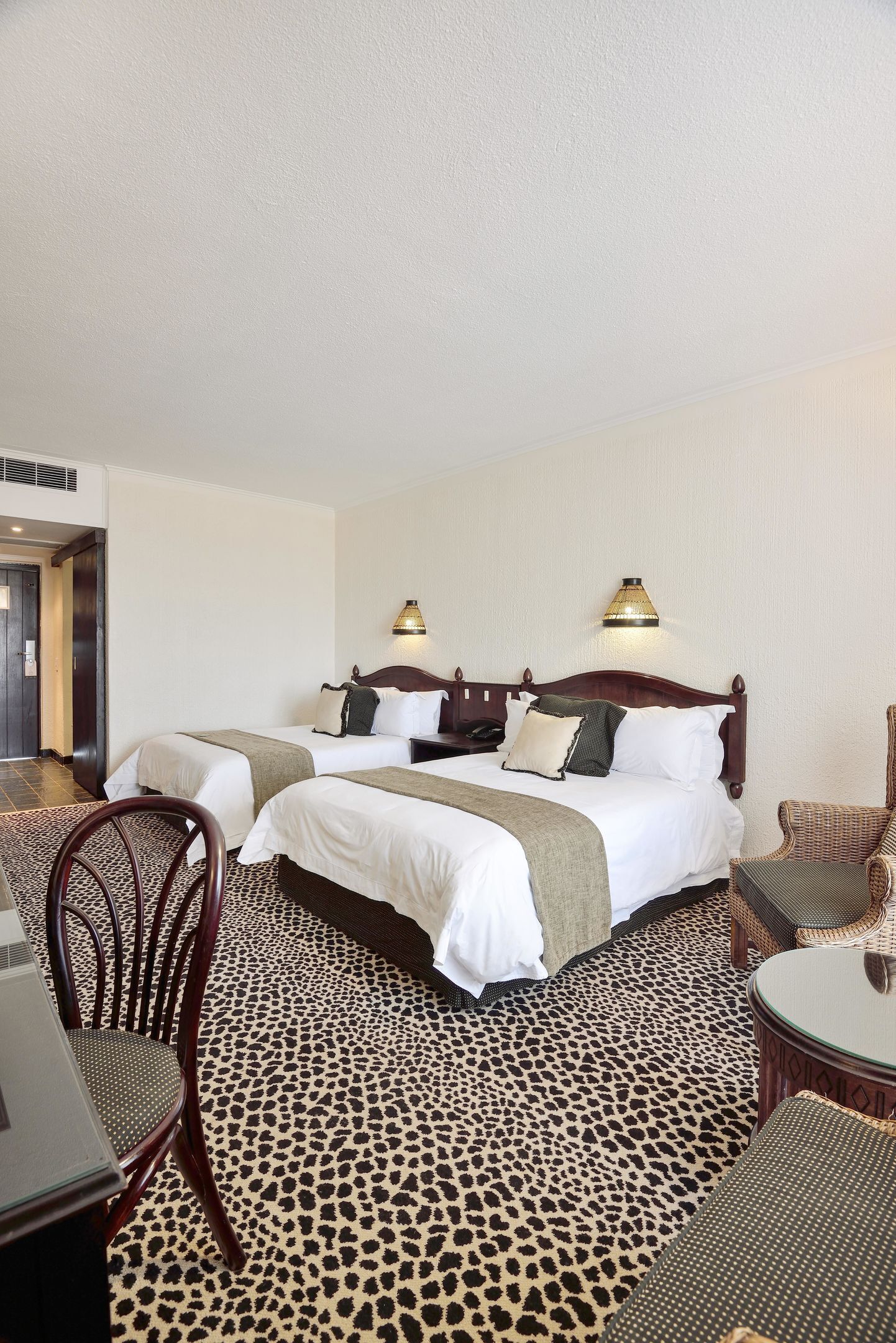 A hotel room with two beds, a dining table, chairs, a small table, and a lamp.