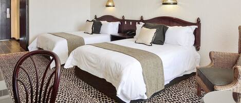 A hotel room with two beds, a dining table, chairs, a small table, and a lamp.