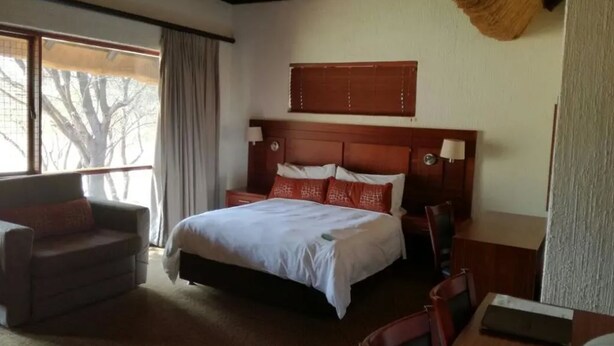 A hotel room with a large bed, a sofa, a desk, and a window with a view of trees.