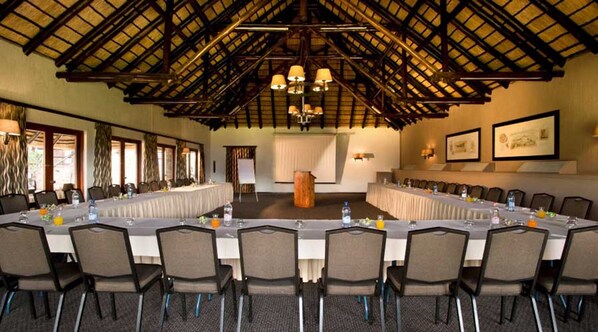 Uma sala de conferências com uma mesa comprida, cadeiras e teto alto com vigas de madeira.