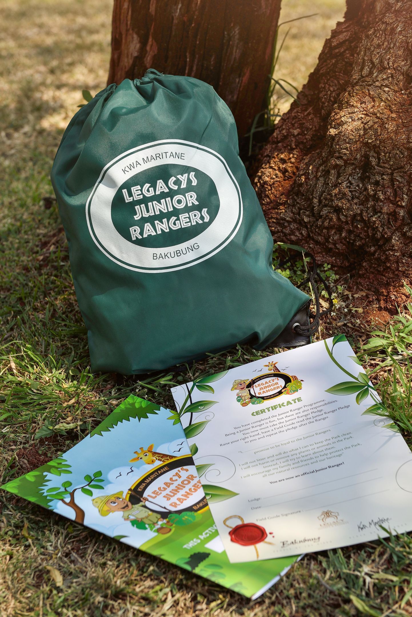 Un sac vert portant l’inscription « Legacy’s Junior Rangers Bakubung » et un certificat posé sur l’herbe.