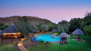 A resort with a swimming pool, thatched-roof structures, and a hillside backdrop.