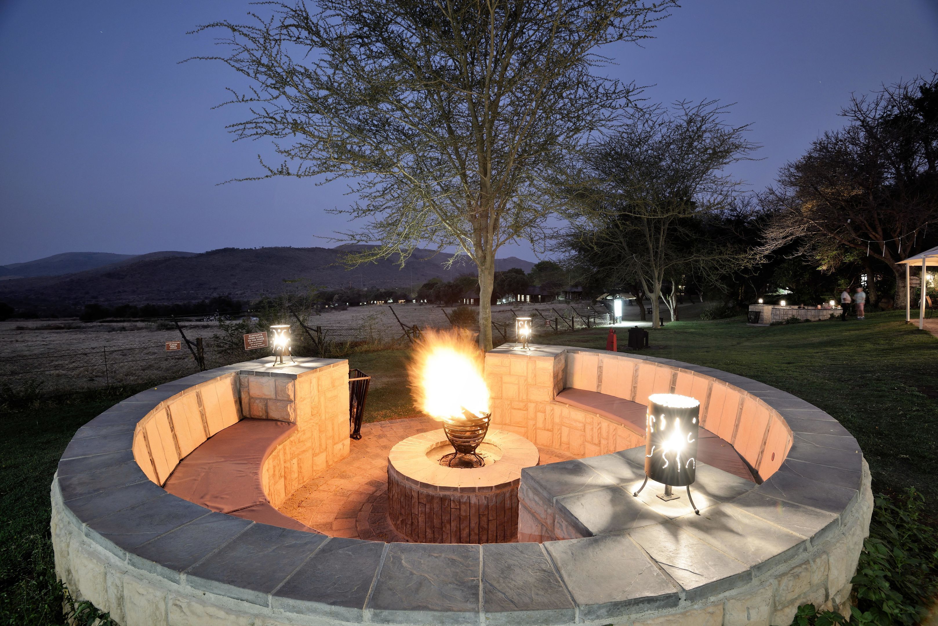 A circular outdoor seating area with a central fire feature, surrounded by stone walls and a tree.
