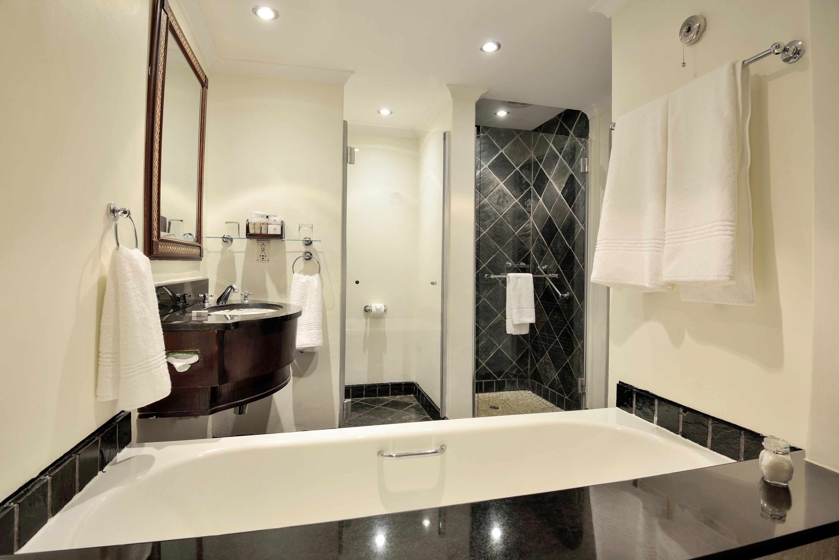 A modern bathroom with a large bathtub, a dark vanity, a glass shower enclosure, and a mirror with a decorative frame.