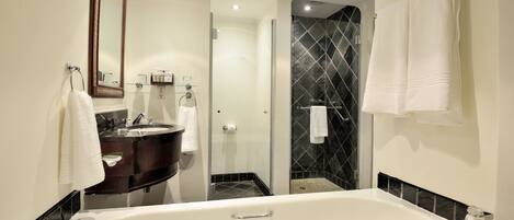 A modern bathroom with a large bathtub, a dark vanity, a glass shower enclosure, and a mirror with a decorative frame.