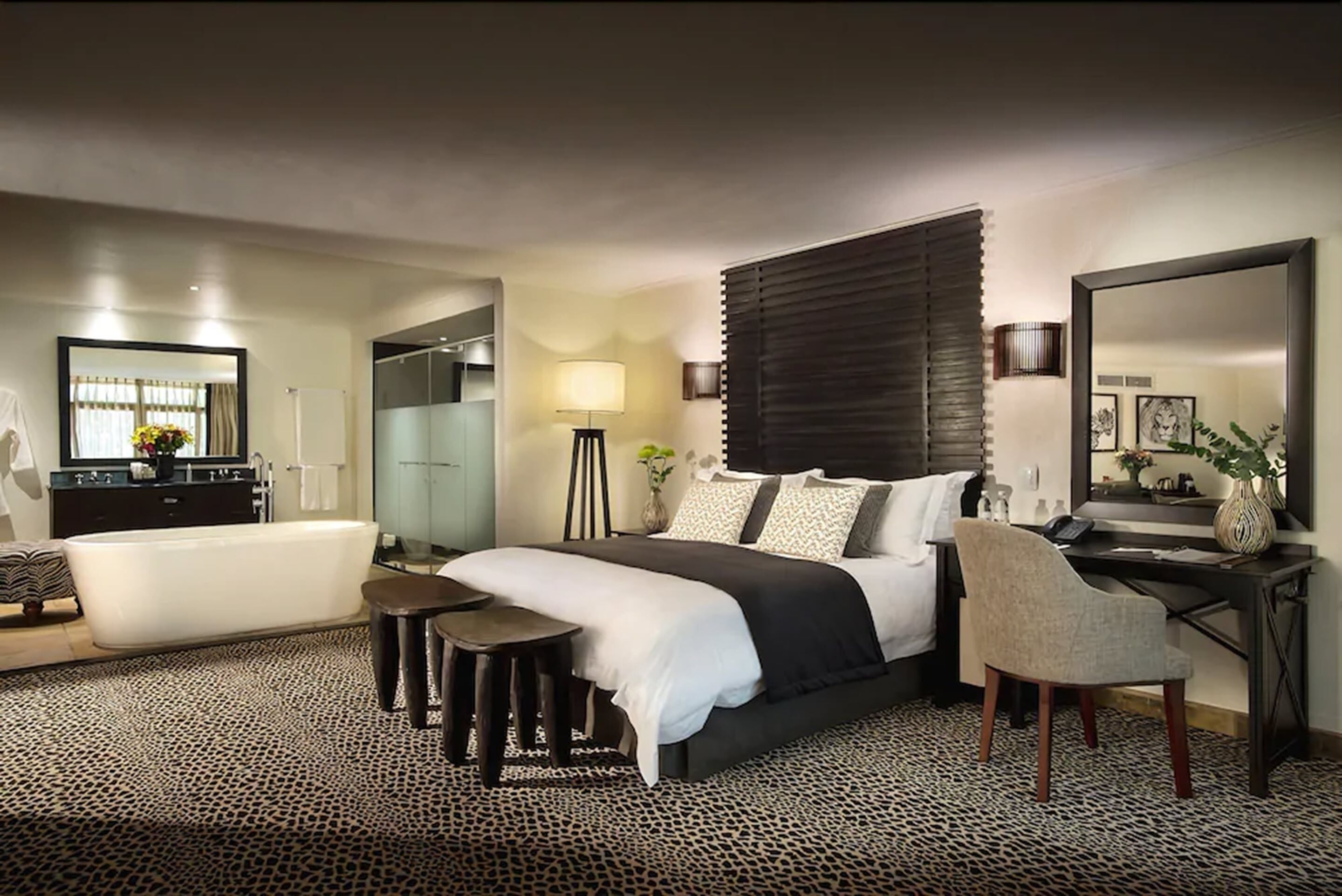 Une chambre d’hôtel moderne dotée d’un grand lit, d’un coin salon avec un canapé et des fauteuils, d’un bureau avec une chaise, d’une baignoire et d’un grand miroir.