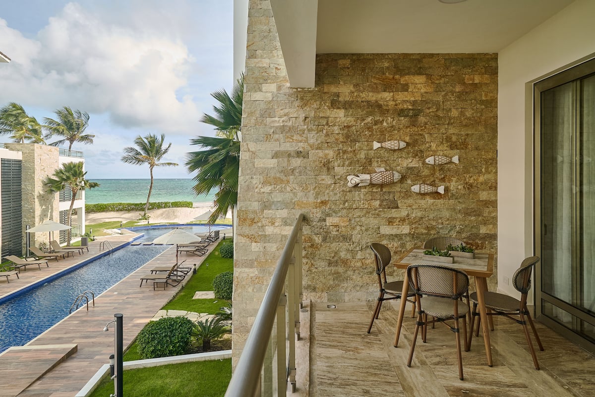 A balcony with a stone wall, a pool, and a view of the beach.