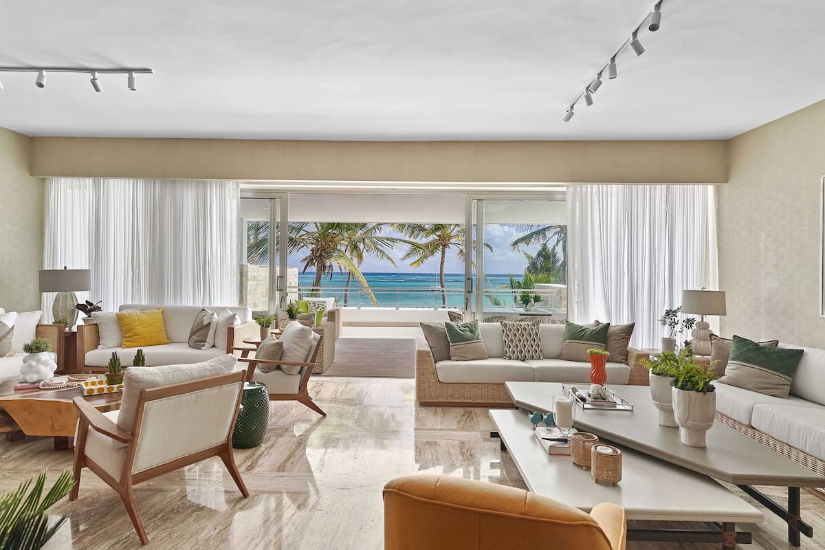 A spacious living room with a large window overlooking the ocean, furnished with a sofa, chairs, and a coffee table.