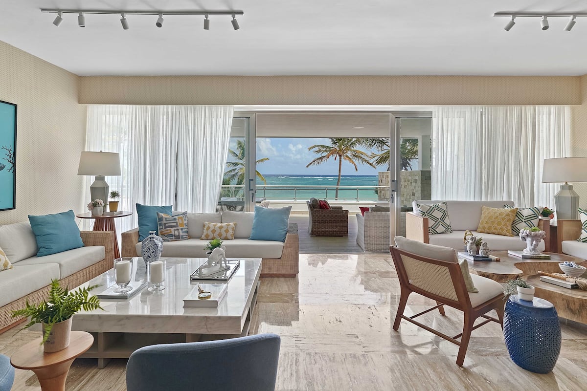 A spacious living room with a large window overlooking the ocean, furnished with a sofa, chairs, and a coffee table.