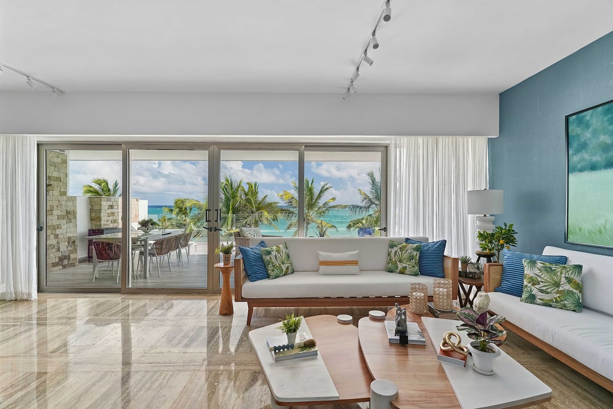 A modern living room with a large sliding glass door leading to a balcony with a view of the ocean.