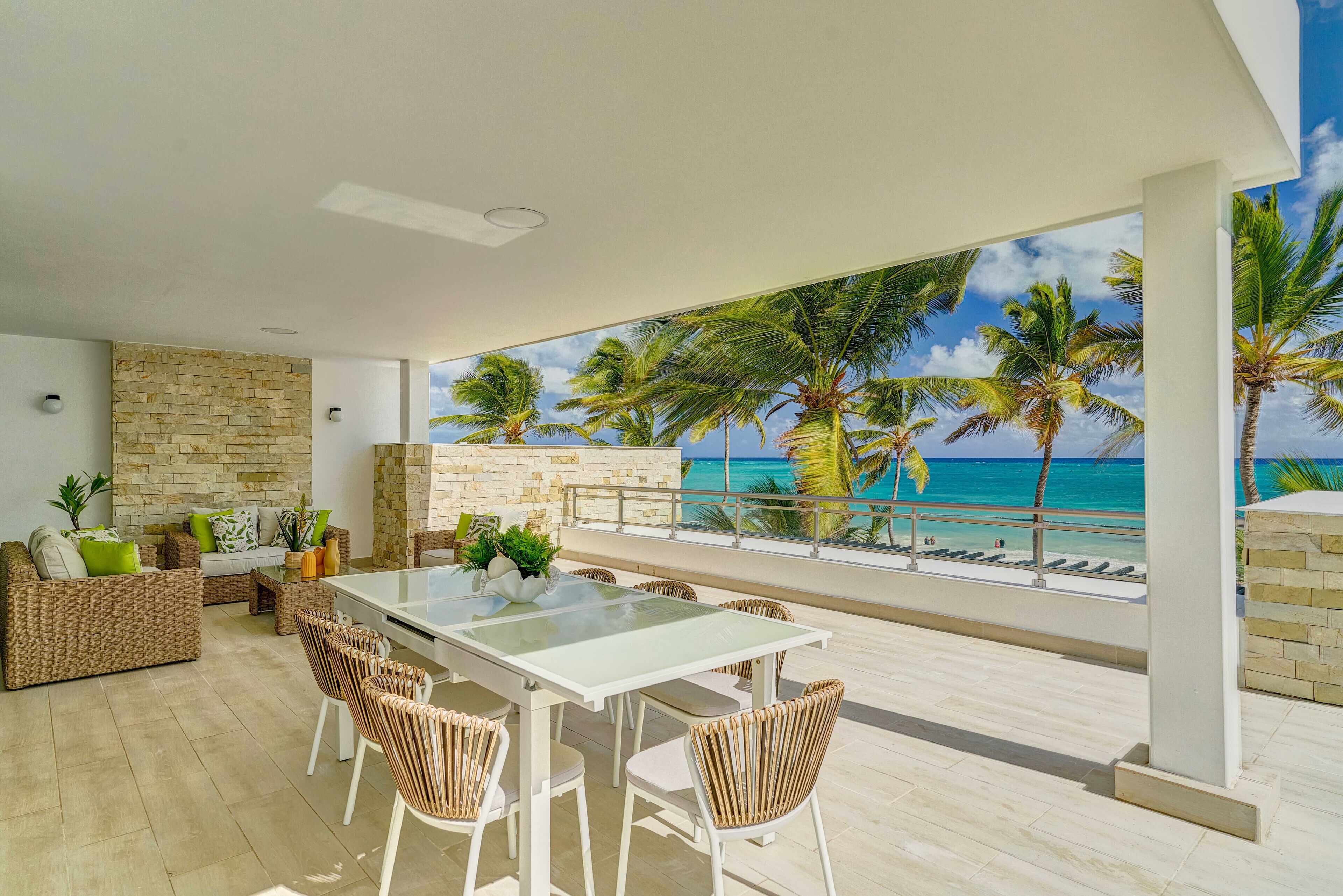 Un espacio exterior moderno con una mesa de vidrio, muebles de mimbre y vista al océano.