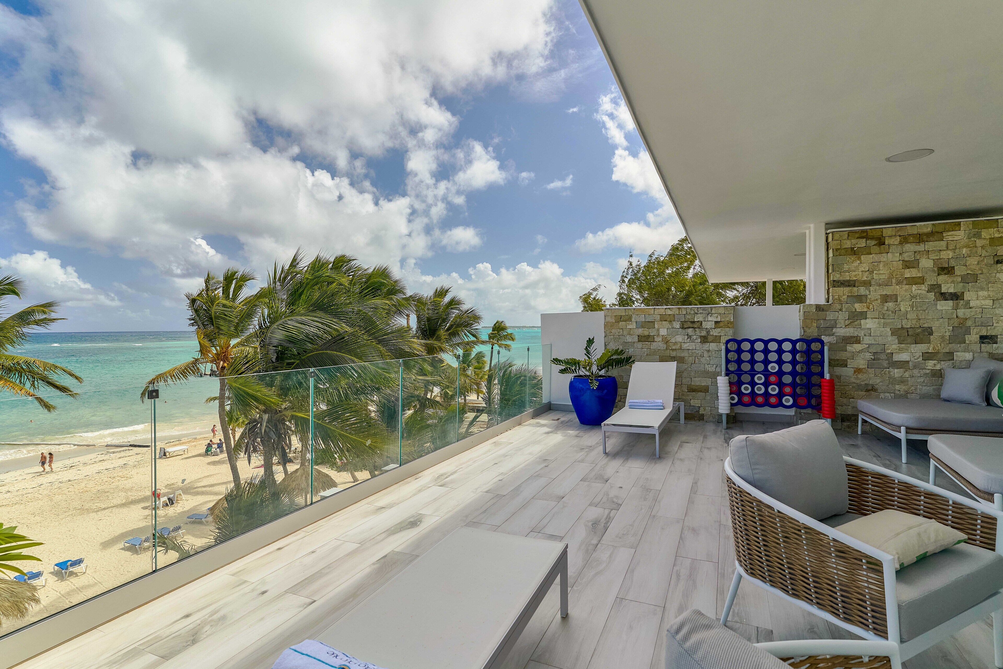 A balcony with a view of the beach, wicker furniture, and a stone wall.