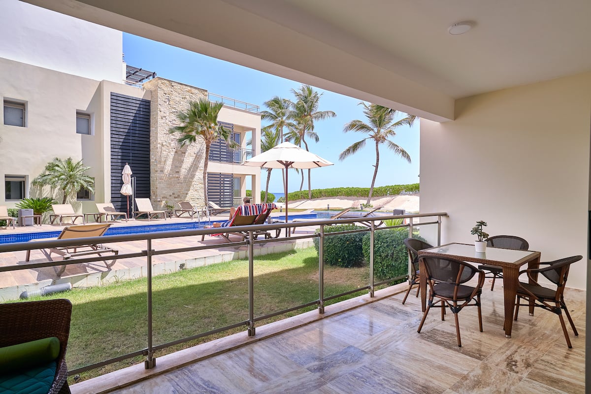 A balcony with a pool, lounge chairs, and a dining area with chairs and a table.