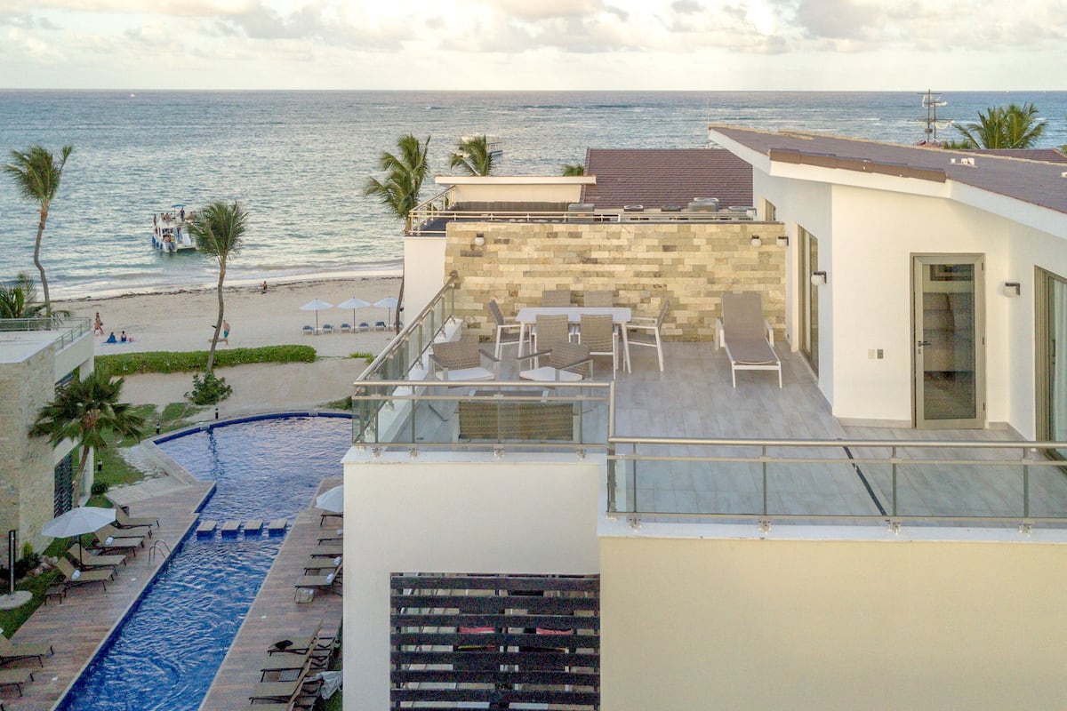 A rooftop pool area with lounge chairs and umbrellas, overlooking a beach and the ocean.