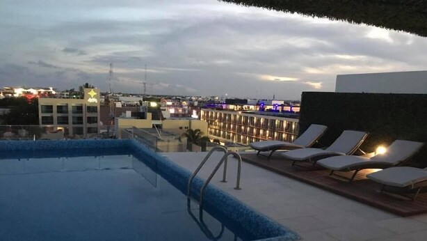 Una piscina en la azotea con sillones de descanso y vistas del paisaje urbano al anochecer.