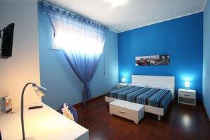 A bedroom with a bed, bedside tables, a desk, a lamp, and a window with curtains.