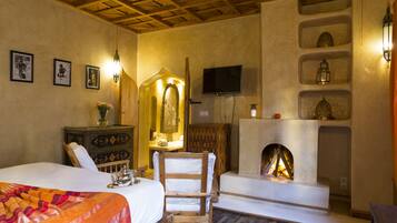 A cozy room with a bed, a wooden chair, a fireplace, and a television on the wall.