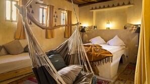 A room with a bed, a hanging chair, a sofa, and a window with curtains. - Riad Chbanate (Essaouira)