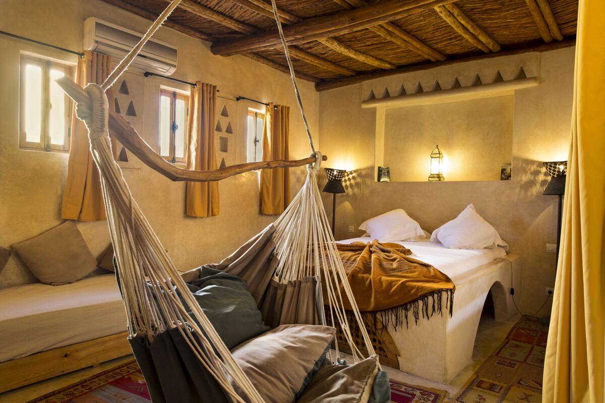 Una habitación con una cama, una silla colgante, un sofá y una ventana con cortinas.
