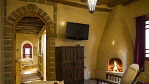 A room with a fireplace, a television mounted on the wall, and a bed with a red blanket. - Riad Chbanate (Essaouira)