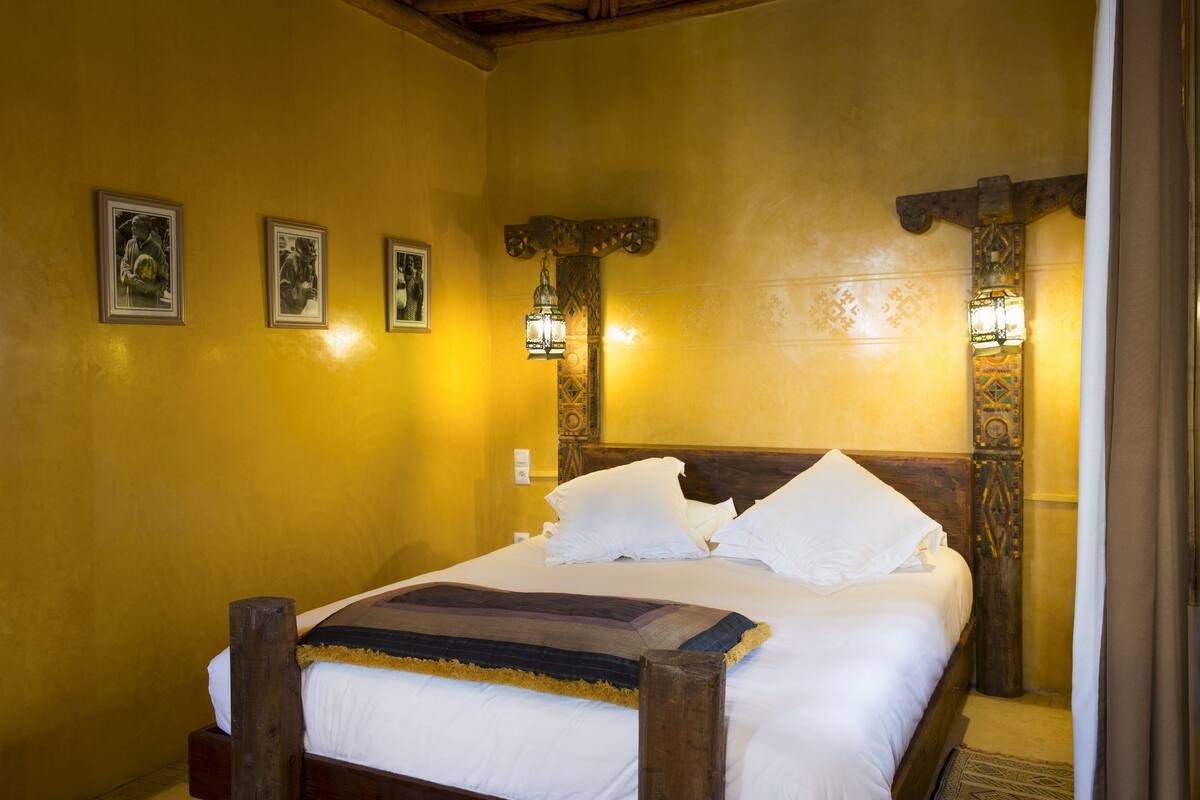 Una cama con sábanas blancas, cabecera de madera y un tapiz decorativo.