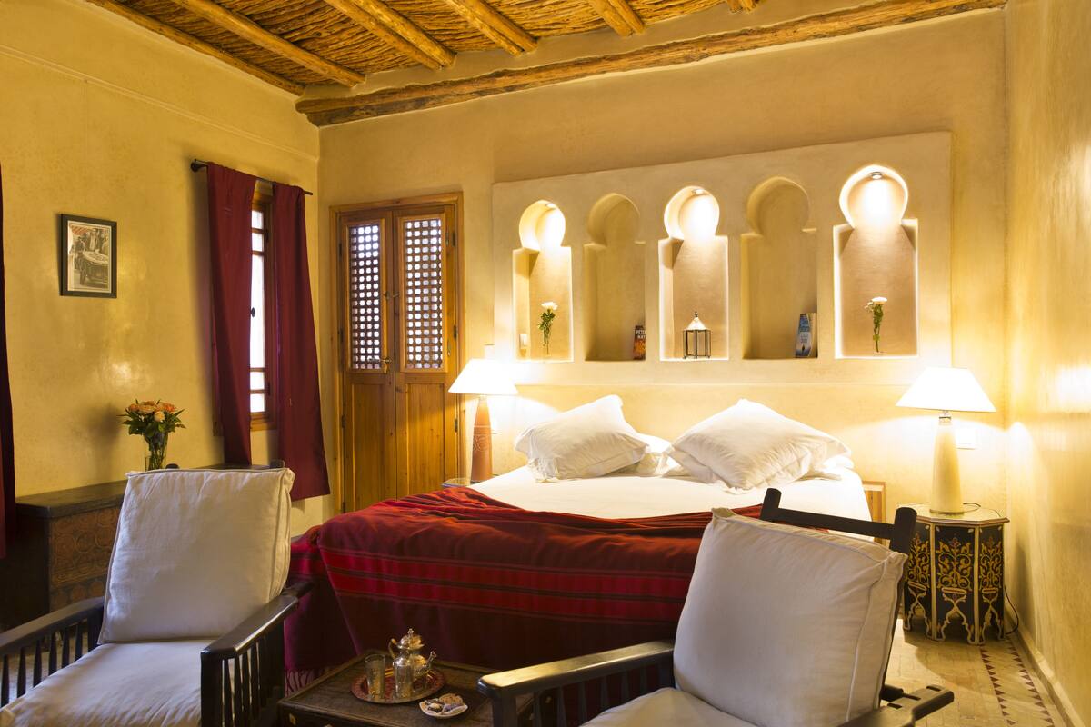 Habitación de hotel con cama, dos sillas, una mesa con bandeja, un espejo y techo de madera.