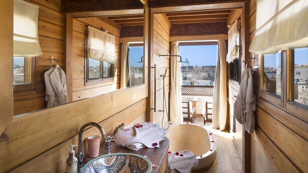 A wooden cabin bathroom with a wooden sink, a bathtub, and a window overlooking a cityscape. - Riad Chbanate (Essaouira)