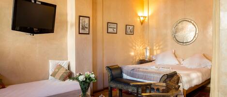 Habitación de hotel con dos camas, televisión, lámpara de pared y una mesita con un jarrón de flores.