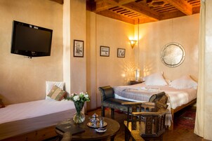 Habitación de hotel con dos camas, televisión, lámpara de pared y una mesita con un jarrón de flores.
