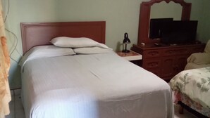 Ein ordentlich bezogenes Bett mit einem Holz-Kopfteil, ein Nachttisch mit Lampe und ein Fernseher auf einer hölzernen Kommode.