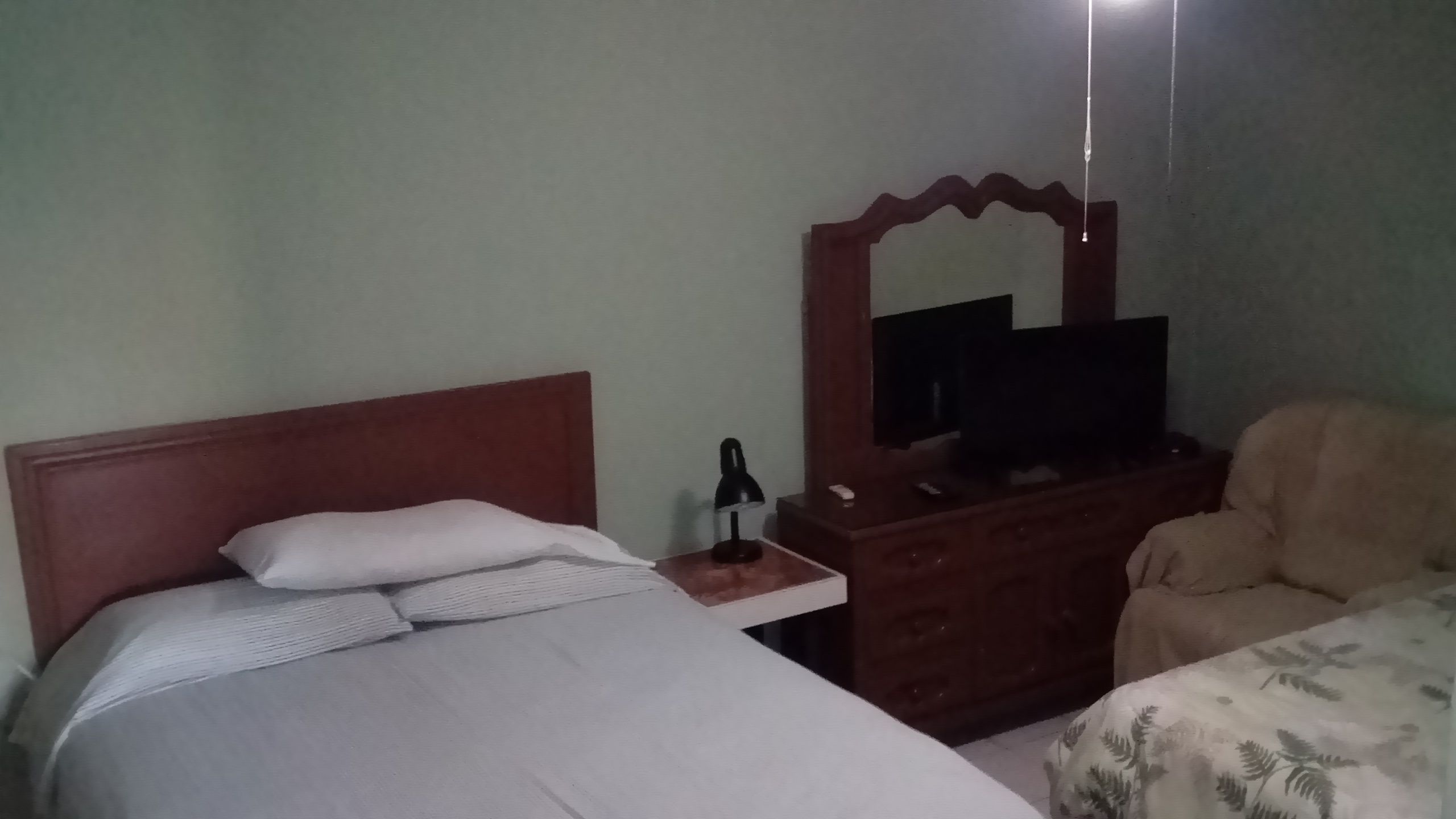 A hotel room with a bed, a wooden dresser, a television, and a chair.