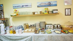 Monipuolinen aamiaisbuffet, jossa on tarjolla erilaisia ruokia, ruokailuvälineitä ja kahvipiste.