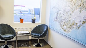 Huoneessa on kaksi tuolia, pöytä, jonka päällä on kirja, ikkuna, josta avautuu näkymä huoltoasemalle, ja suuri kartta seinällä.