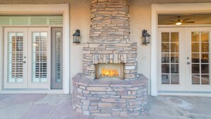 A stone fireplace with a fire, flanked by two doors with glass panels and exterior lighting fixtures. - Casa Delight (Scottsdale)