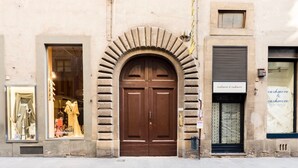 A building facade with a central arched entrance, two side windows with mannequins, and a sign above the right window. - "Botticelli","Donatello"&"Dante"apartments by WP Relais in the heart of Florence (Firenze)