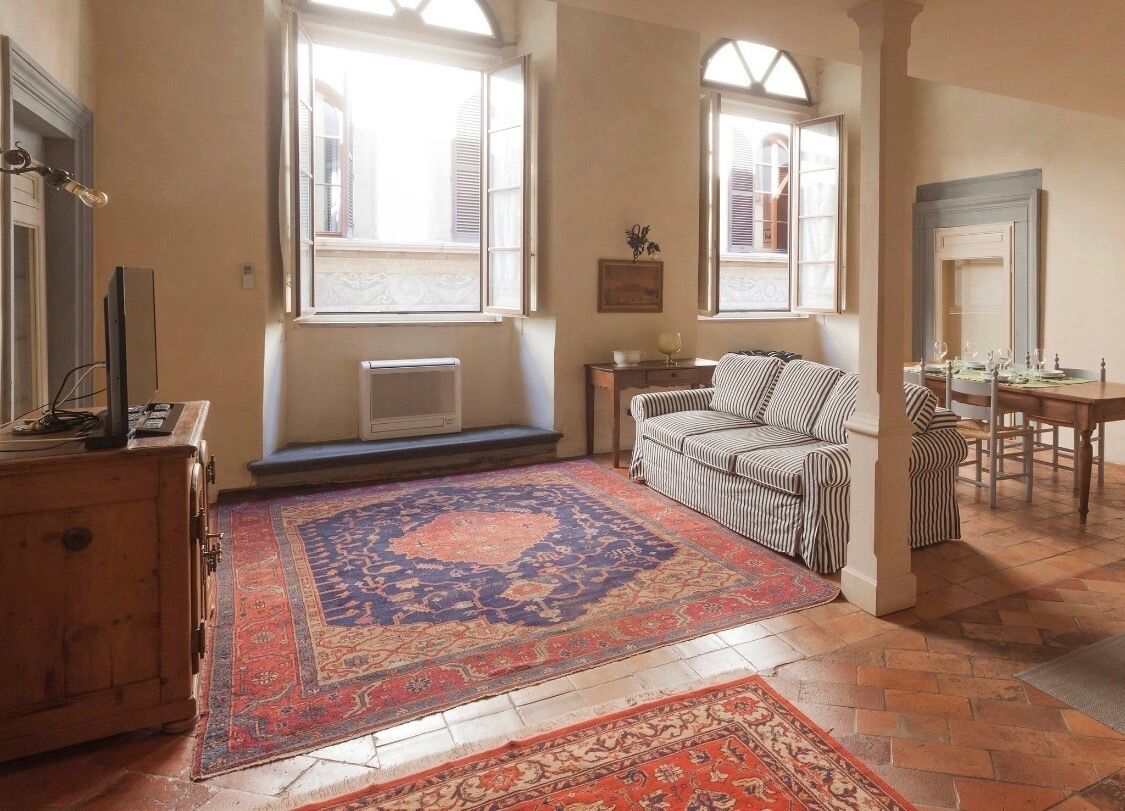 A cozy room with a large patterned rug, a striped sofa, a dining table with chairs, and a wooden cabinet.