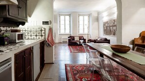 A spacious kitchen with a dining area, featuring a large island, dark wooden cabinets, and a view through an archway to a living room with a sofa and a fireplace. - "Botticelli","Donatello"&"Dante"apartments by WP Relais in the heart of Florence (Firenze)