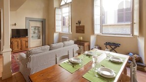 A dining area with a wooden table set for four, a striped sofa, and a television in the background. - "Botticelli","Donatello"&"Dante"apartments by WP Relais in the heart of Florence (Firenze)