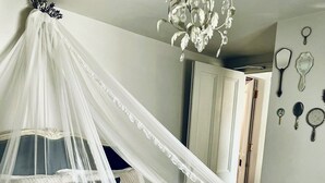 Quarto com cama de dossel, um candelabro e uma parede decorada com vários objetos.