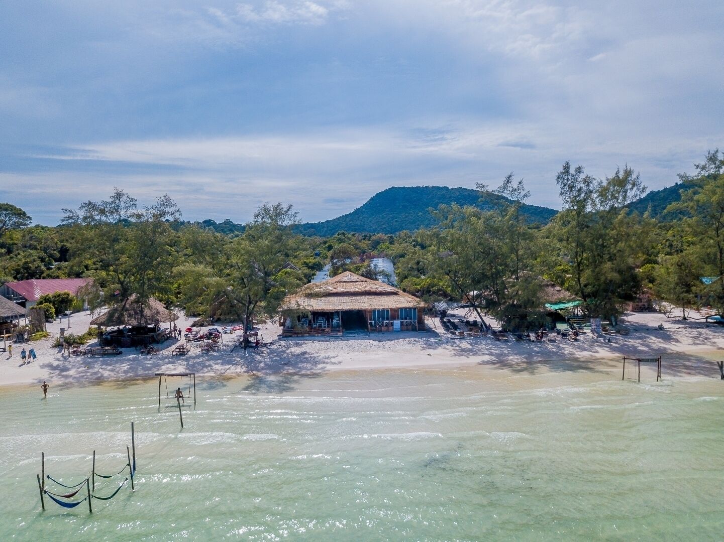 A beachside resort with a thatched-roof building, clear turquoise waters, and lush greenery.