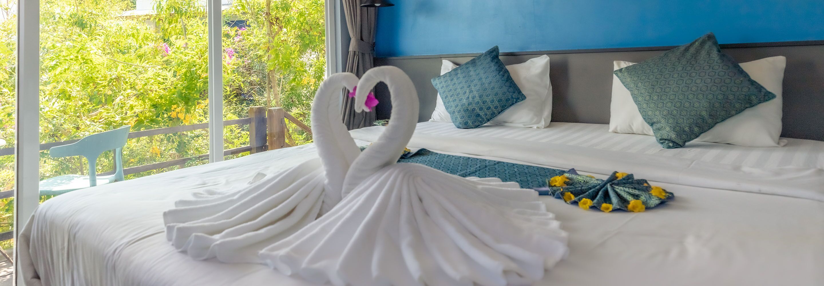 Une chambre d’hôtel avec un lit agrémenté d’une couvre-lit en forme de cygne, une vue sur la verdure par la fenêtre et un mur bleu.