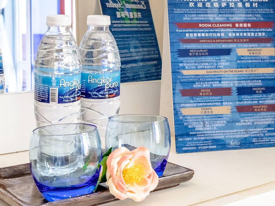 A hotel reception area with a glass display of water bottles, a tray with glasses and a rose, and a multilingual informational board.
