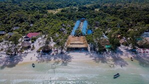 An aerial view of a coastal resort with a beach, thatched-roof huts, and a row of blue-roofed buildings. - Sara Resort (Koh Rong Sanloem)