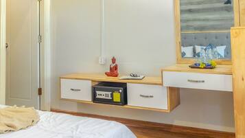 A hotel room with a bed, a wooden wardrobe, a desk with drawers, a mirror, and a small statue.