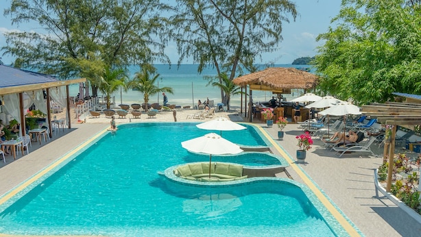 A pool area with lounge chairs and umbrellas, a covered seating area, and a view of the beach. - Sara Resort (Koh Rong Sanloem)